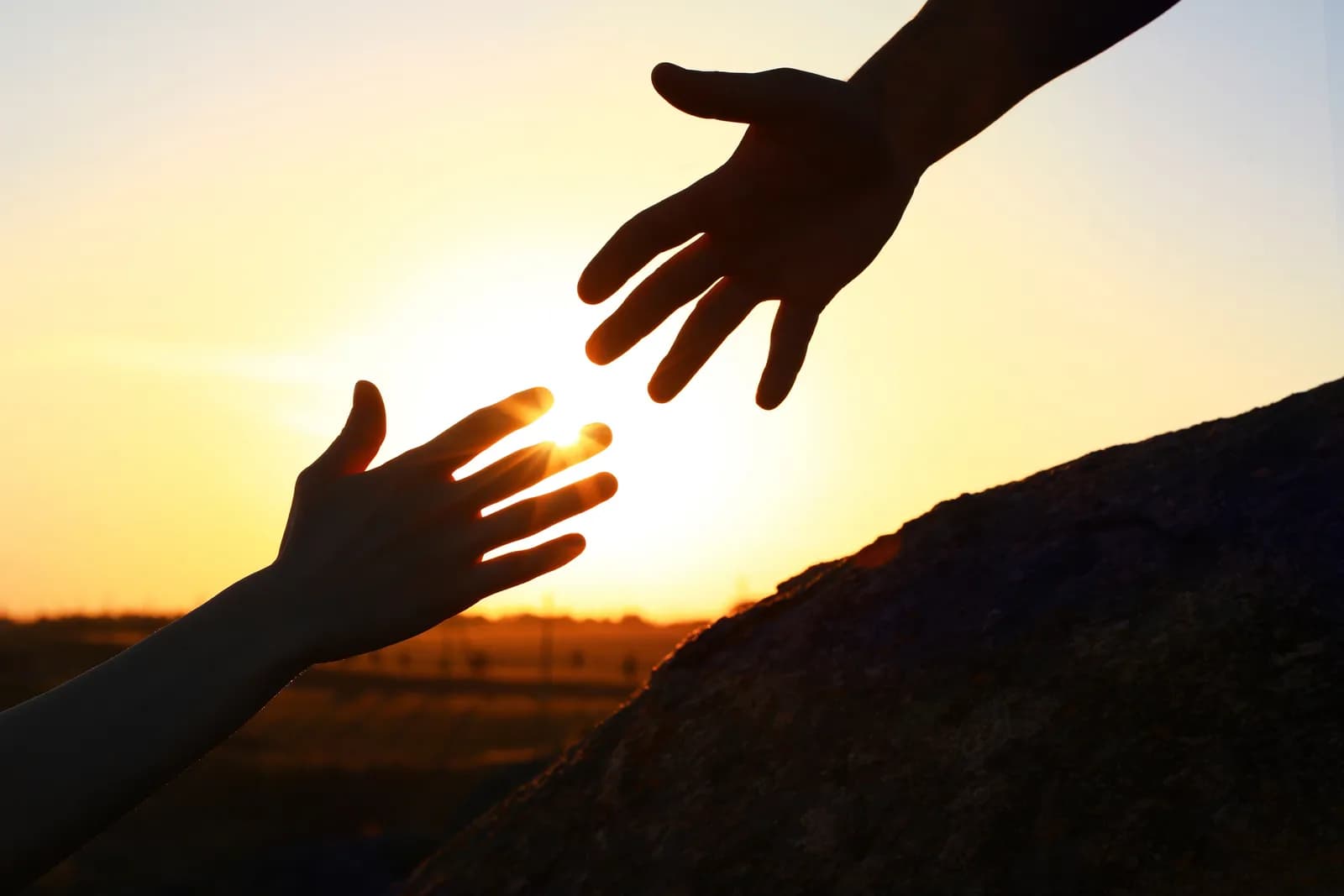 Two hands reaching toward each other against a sunrise